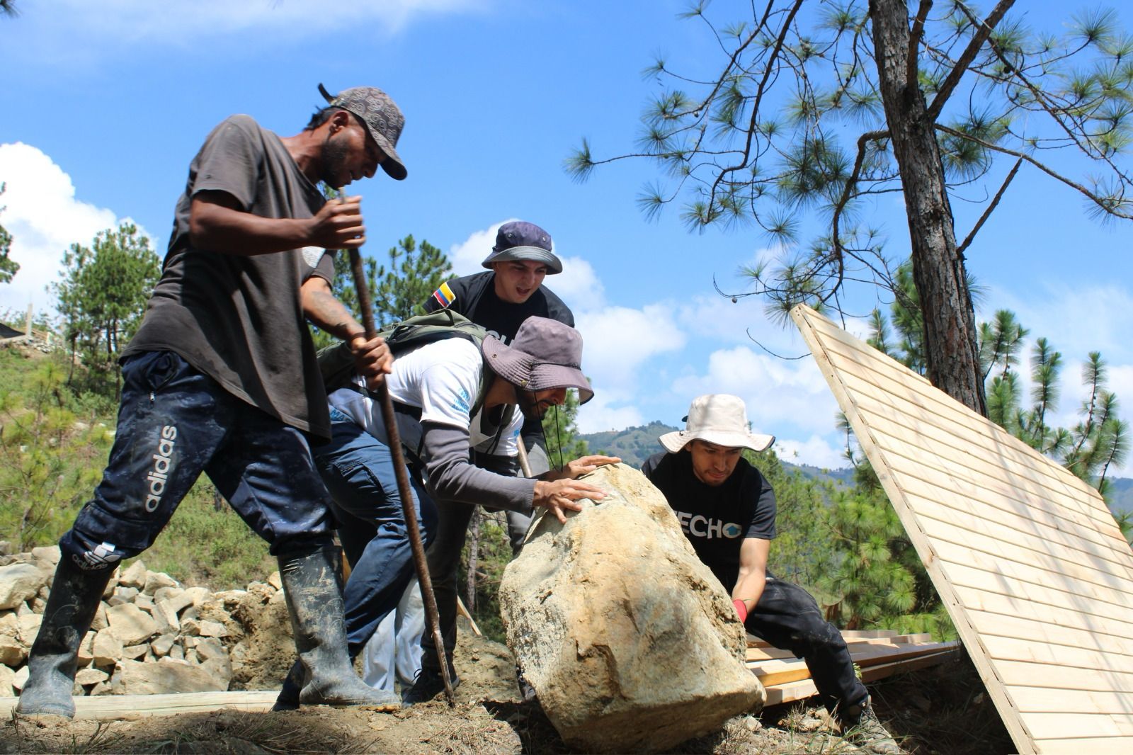 Cuatro voluntarios de TECHO mueven entre todos una piedra grande para despejar el terreno donde se levantará una vivienda.
