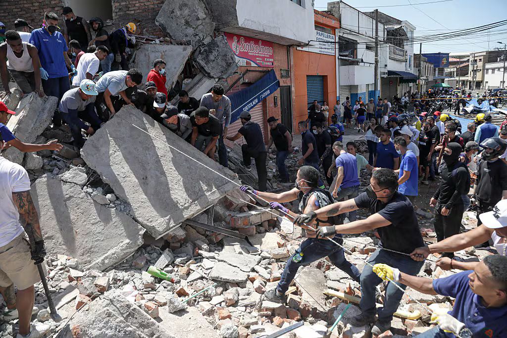 Decenas de personas retiran a mano los escombros de un edificio derrumbado, tirando de una losa de concreto con cuerdas.